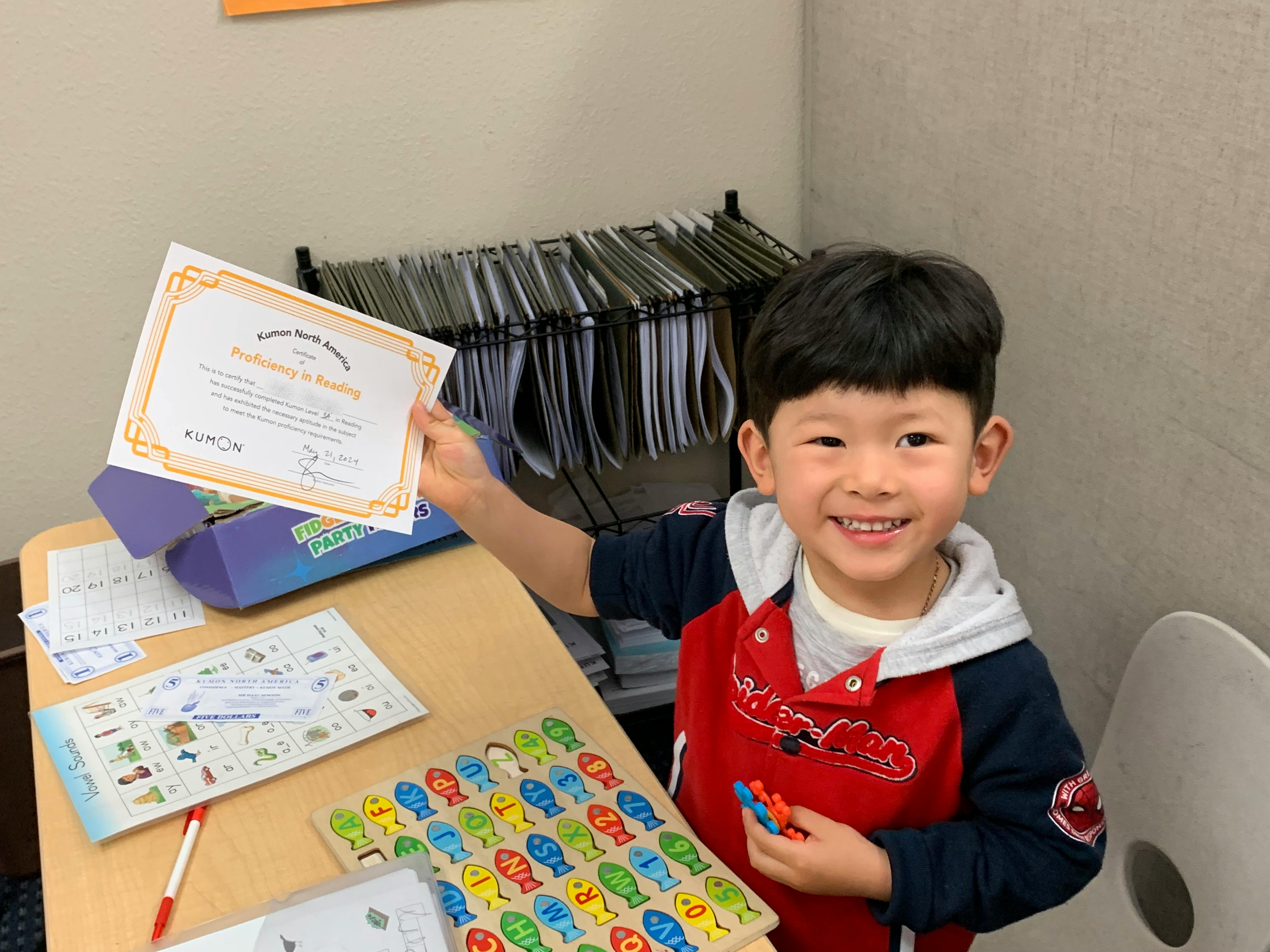 Child smiling while holding up a certificate for "Proficiency in Reading"
