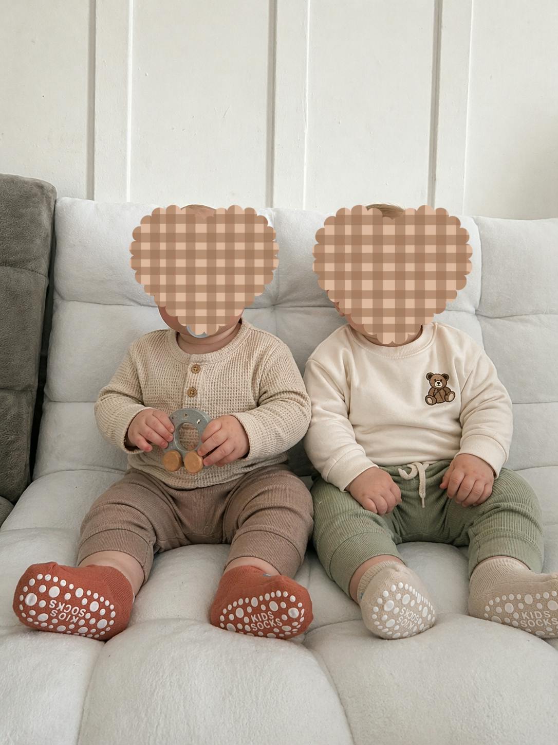 Two babies sitting side-by-side, one holding a wooden toy