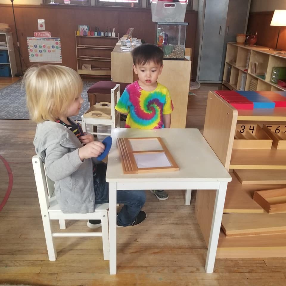 Two children at a small table with a wooden learning toy