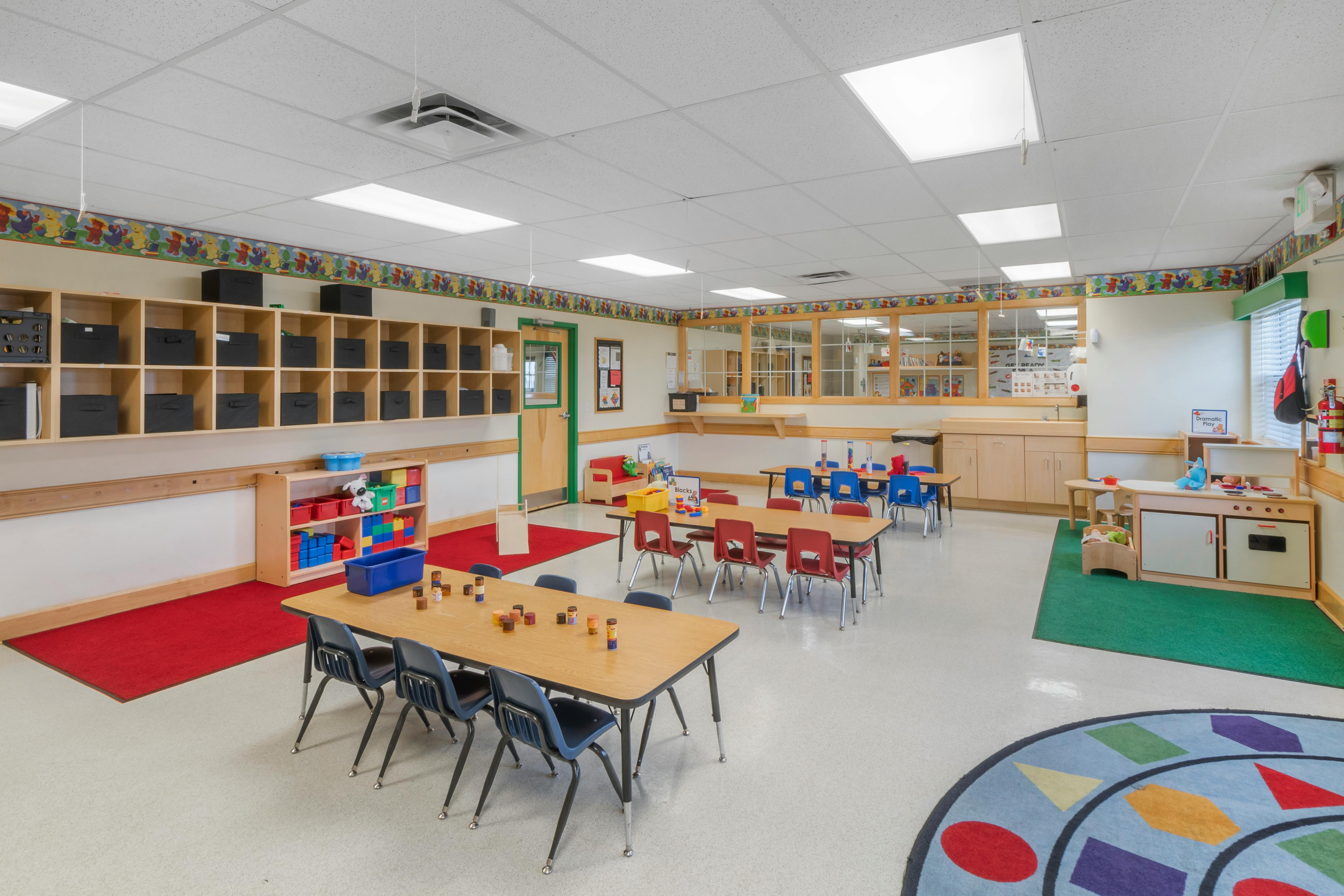 A colorful empty classroom with small tables and chairs arranged, storage cubbies