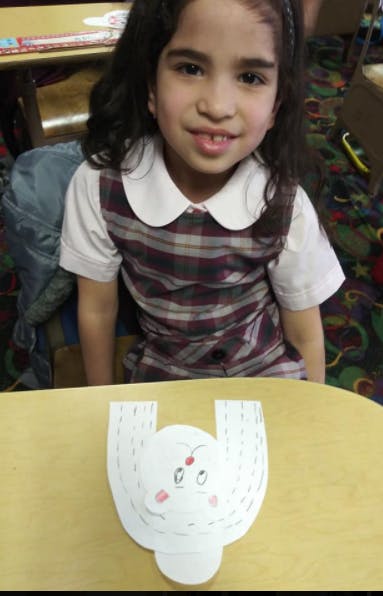 Child in plaid dress with paper craft on table