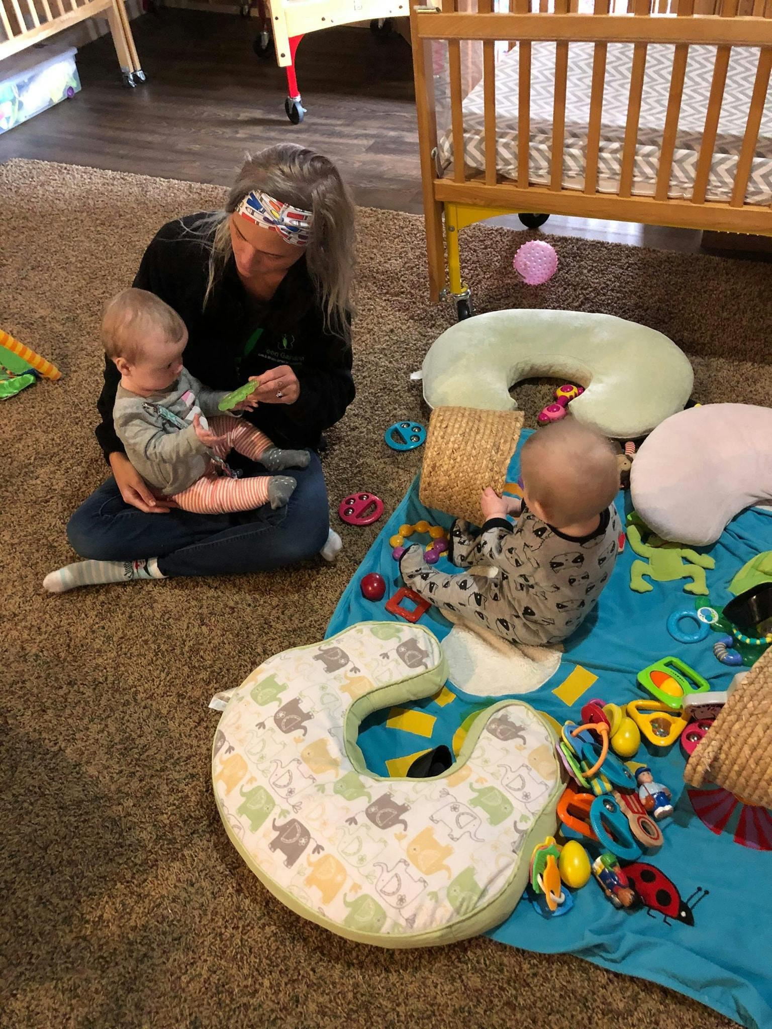 Person holding a child, another child playing on a mat with toys