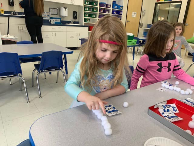 Child playing with cards and cotton balls at a table