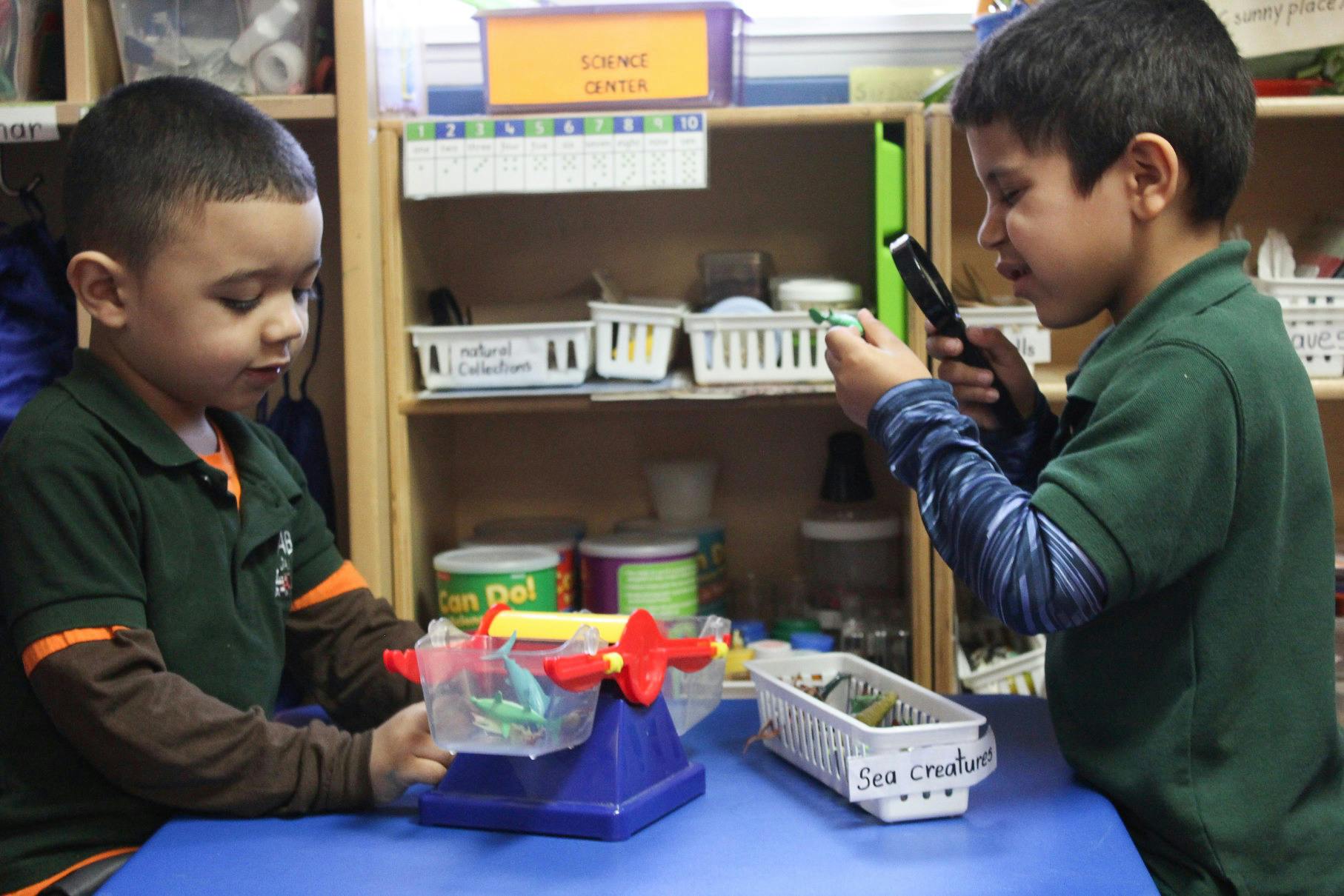 Two children playing with a scale and magnifying glass in a classroom
