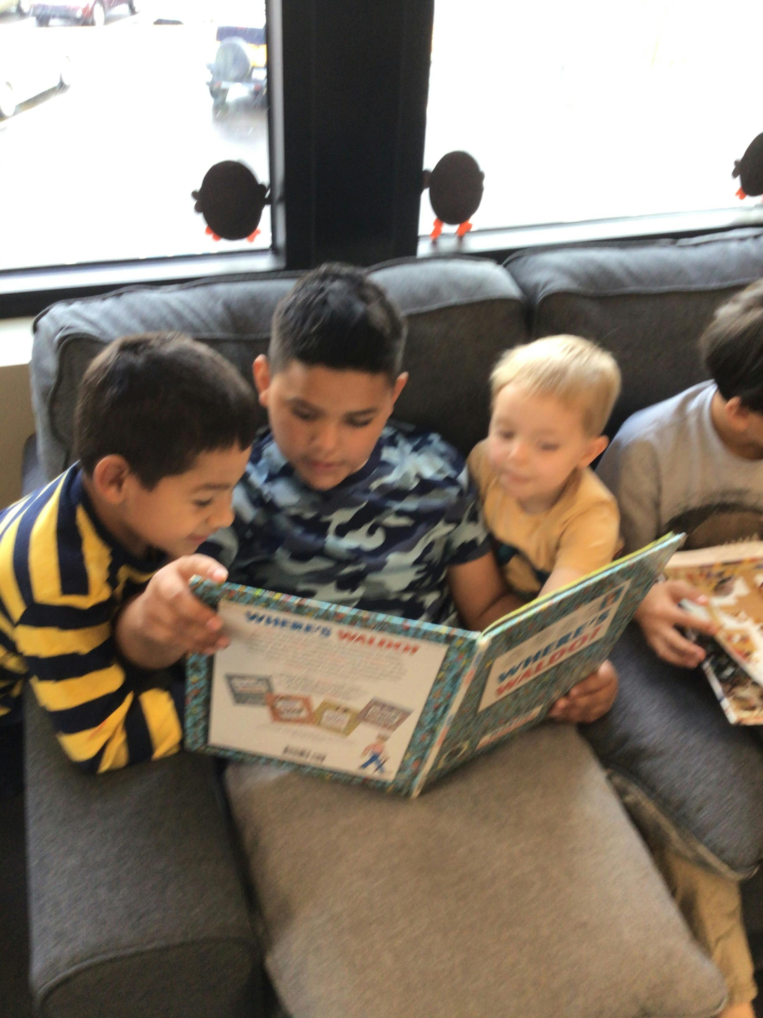 Three children sitting on a couch reading a book together