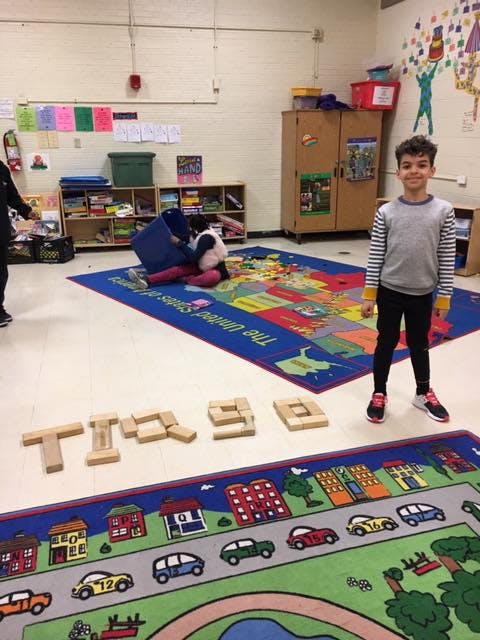Child standing on a rug with another child playing in a classroom
