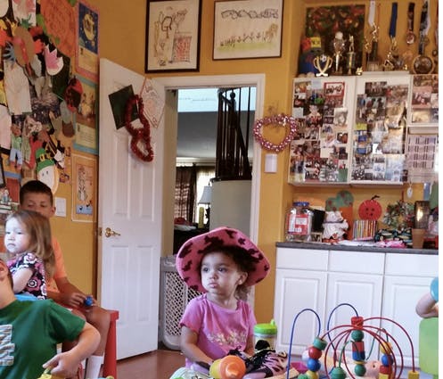 Child in a pink hat playing with a bead maze, other children nearby