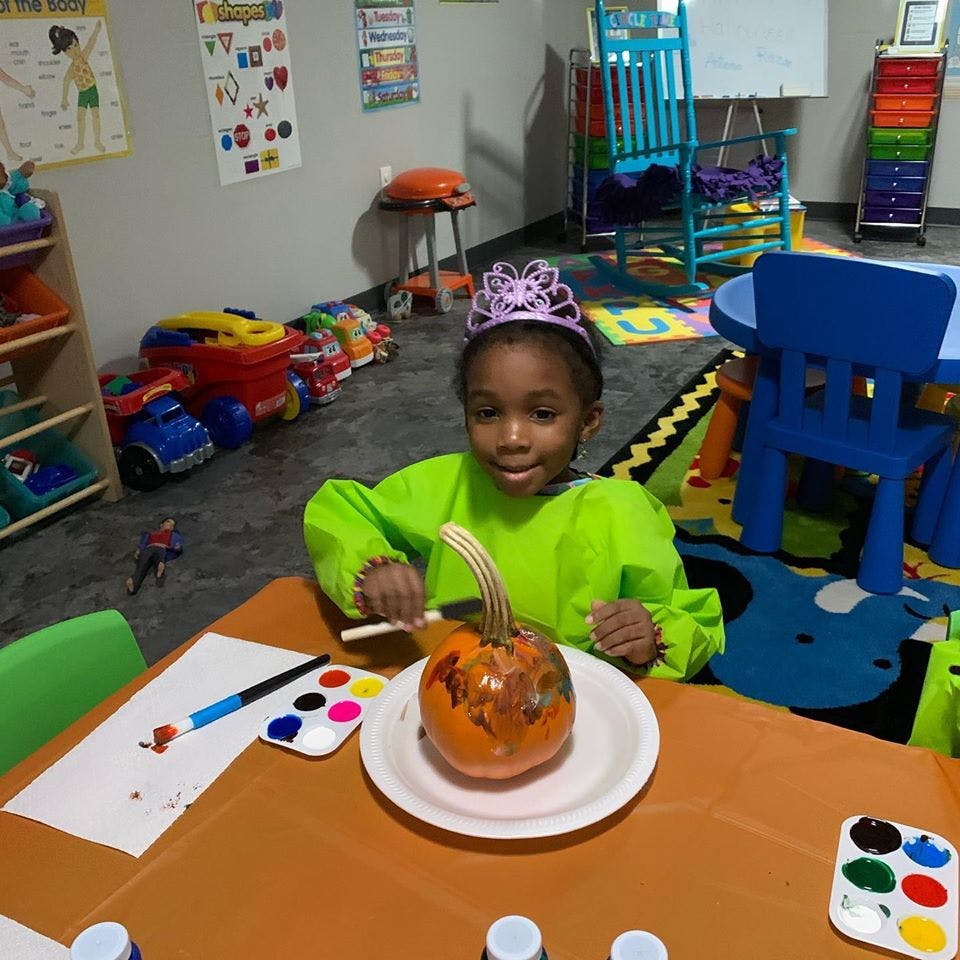 Child in a green smock painting a pumpkin at a table