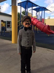 Child in a hat, glasses, and fake mustache standing on a playground