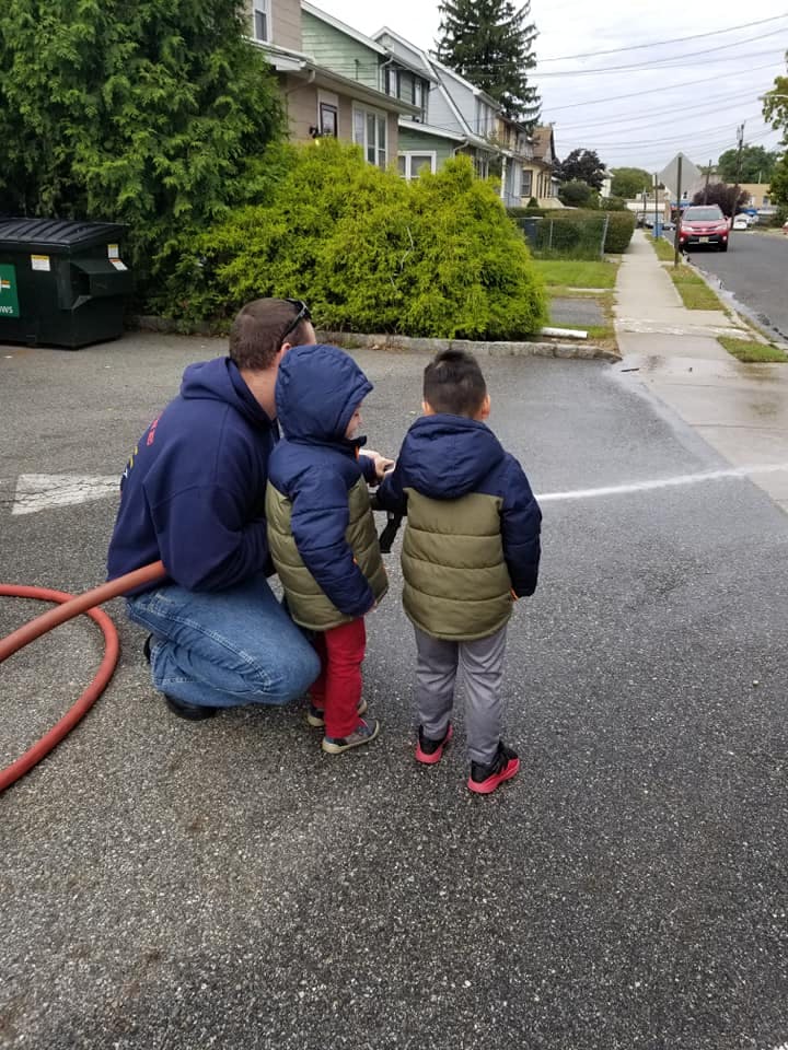 Person kneeling with two children holding a hose