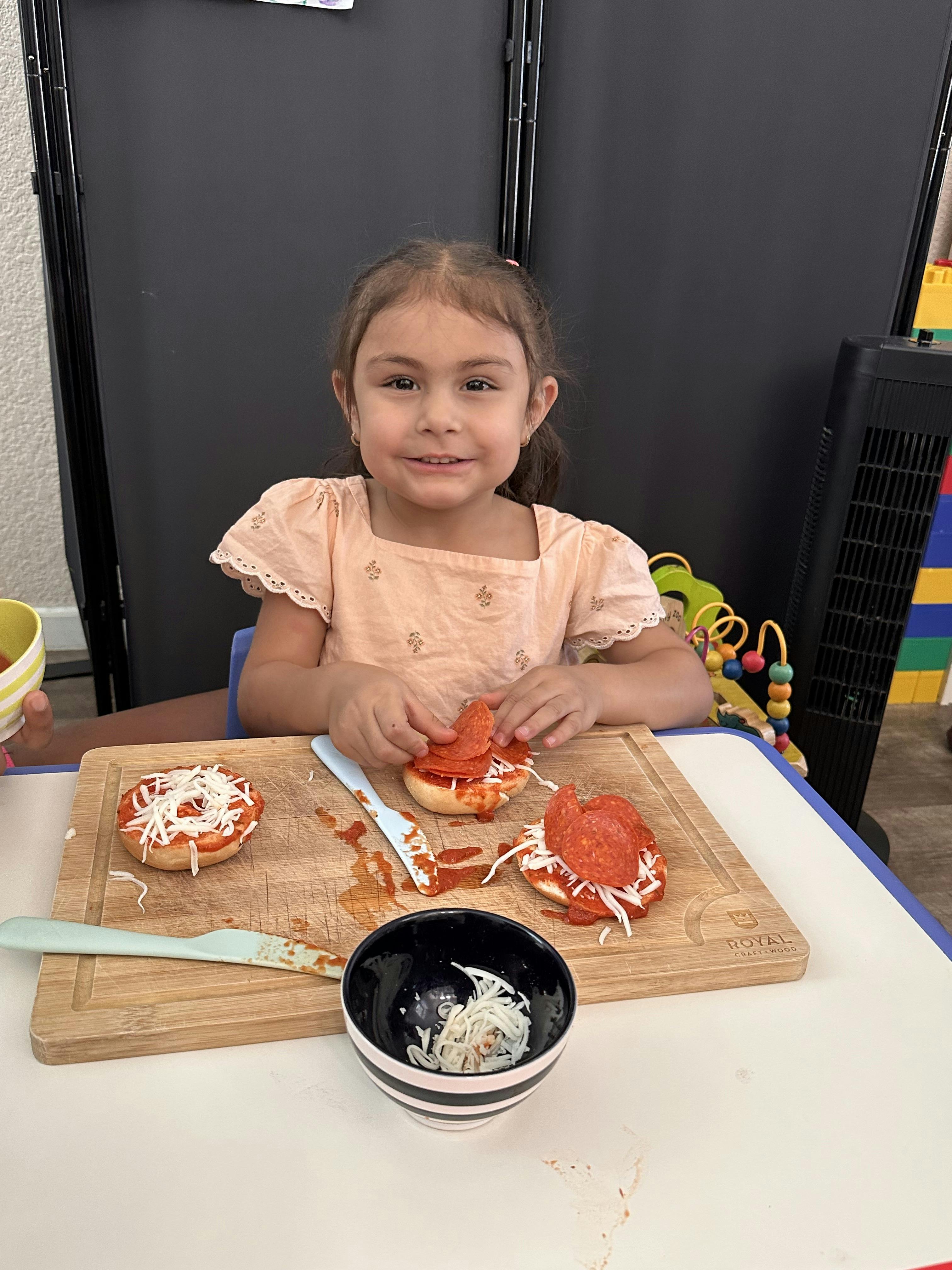 Child placing pepperoni slices on pizza bagels
