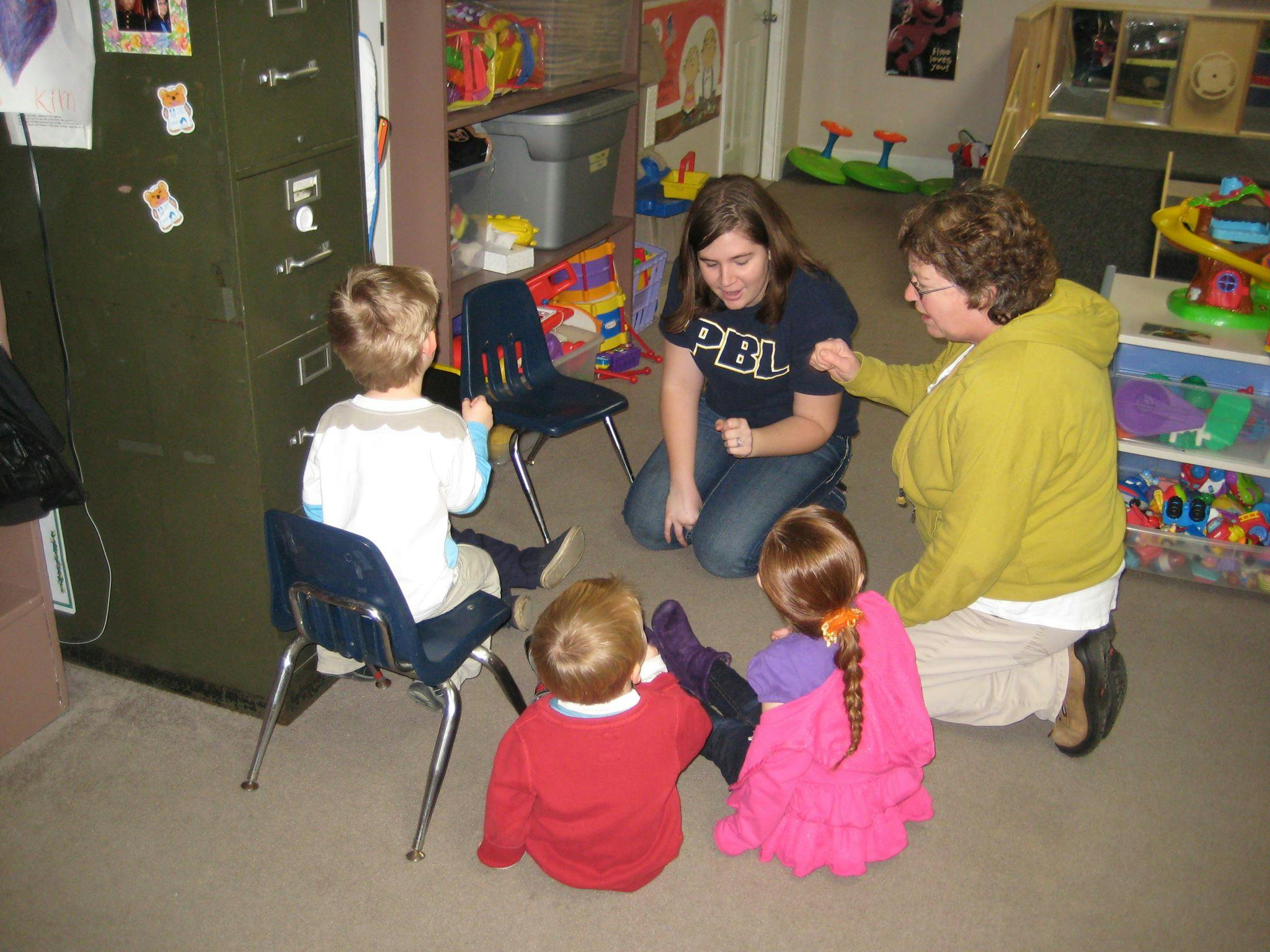 Two adults interacting with three children in a classroom setting