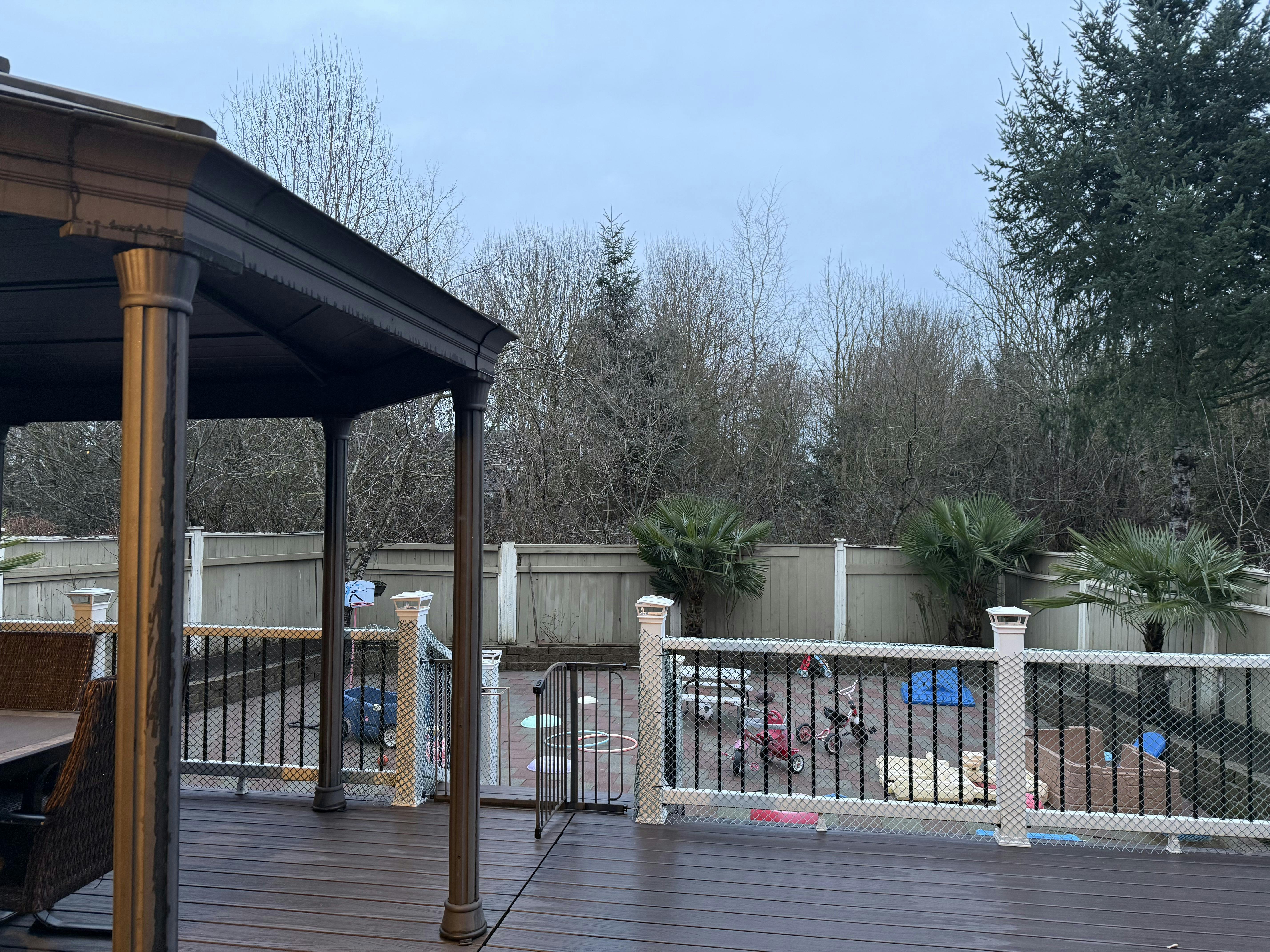 Deck under a gazebo looking out at a fenced yard with children's toys
