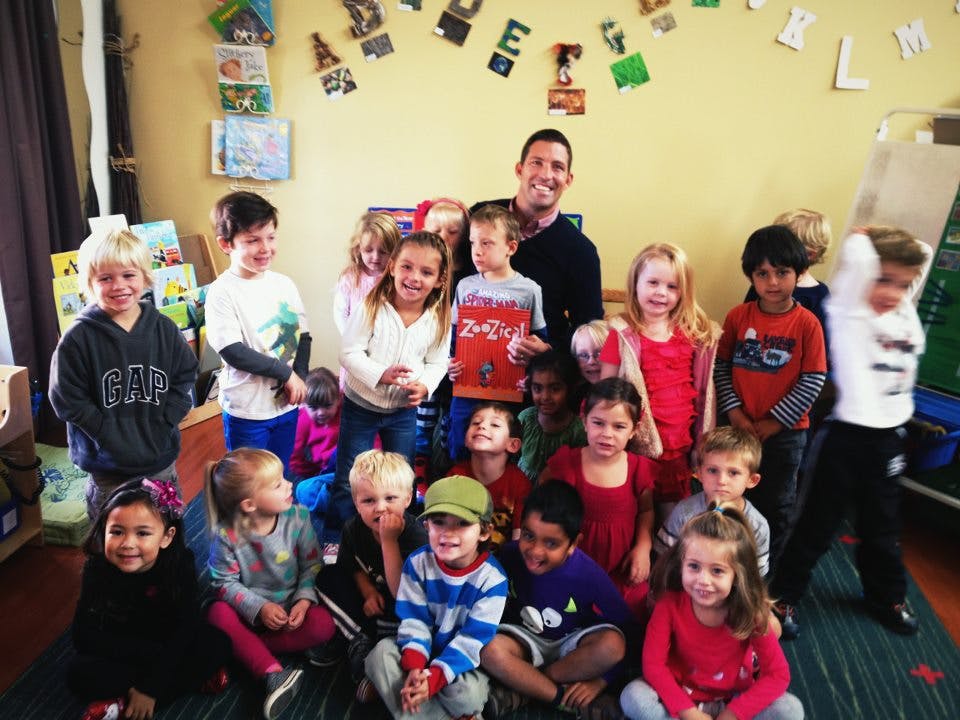 Adult and multiple children posing in a classroom