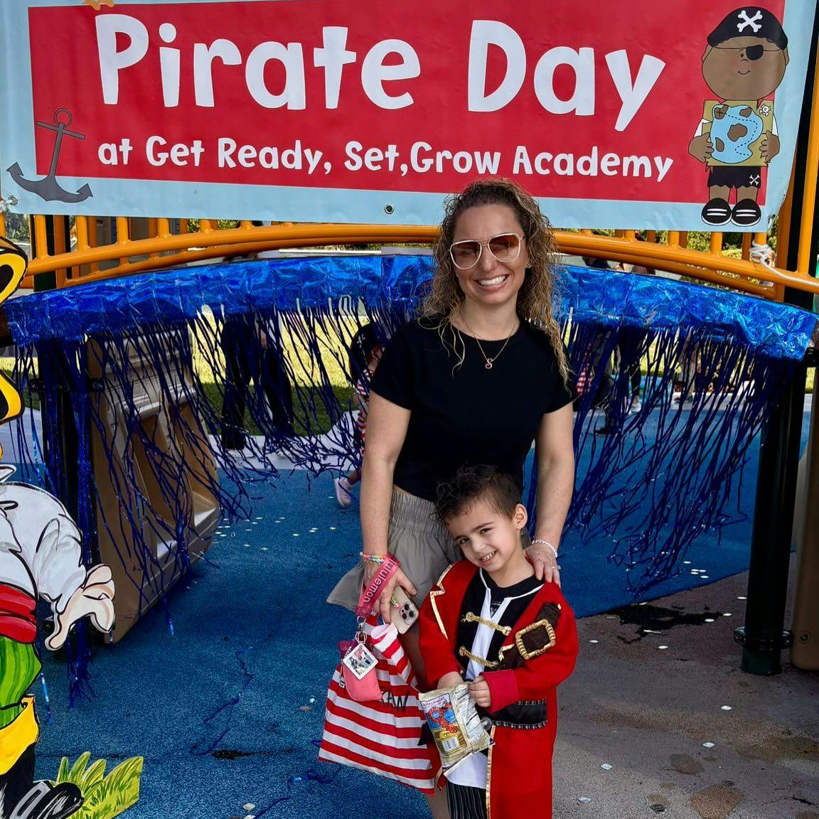 Person and child in pirate costume under a banner that reads "Pirate Day"