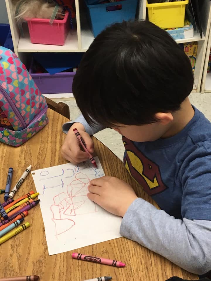 Child drawing on paper with a crayon at a table
