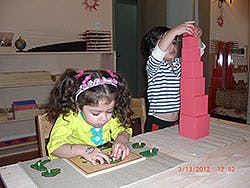 Child playing with puzzle at table, another child stacking blocks