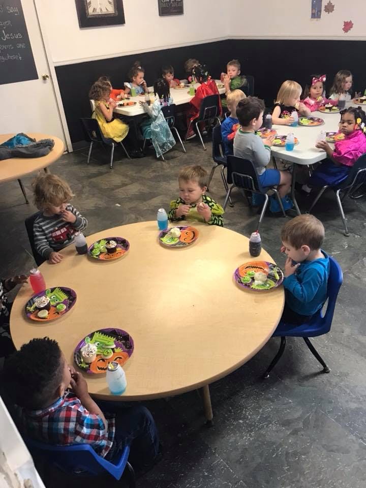 Children sitting at tables eating snacks in a classroom eating snacks