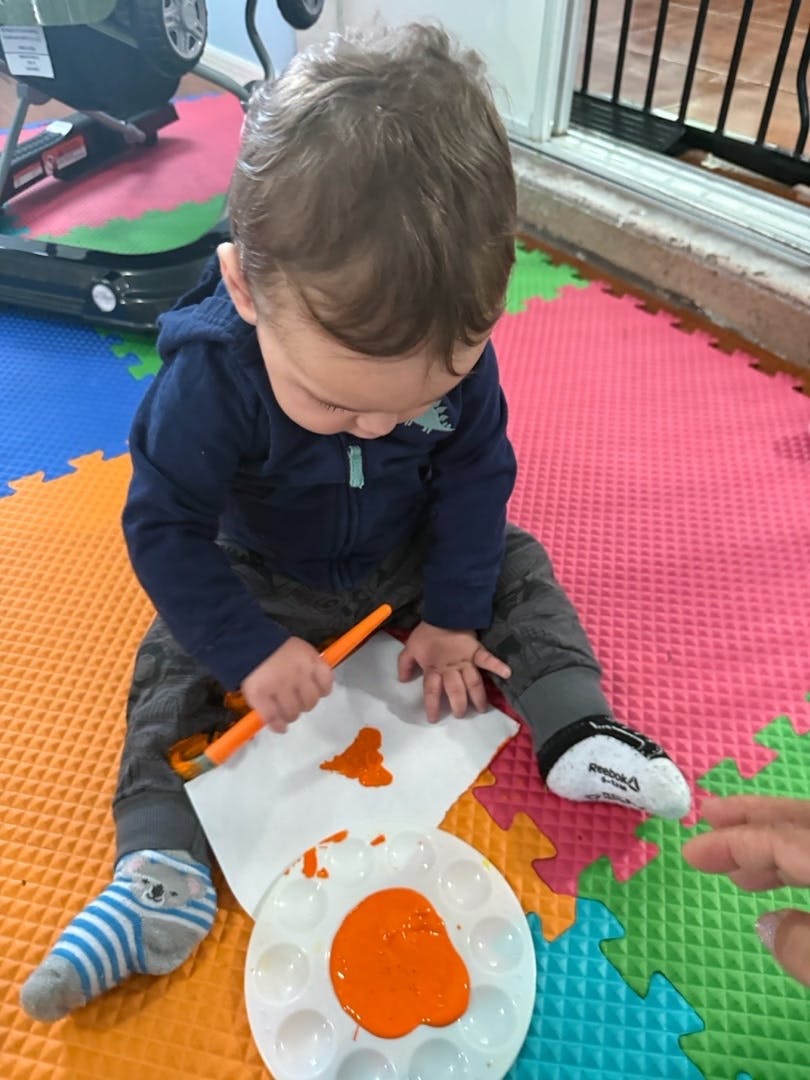 Child painting on paper with orange paint and a paintbrush