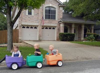 Three children in a toy train on a driveway