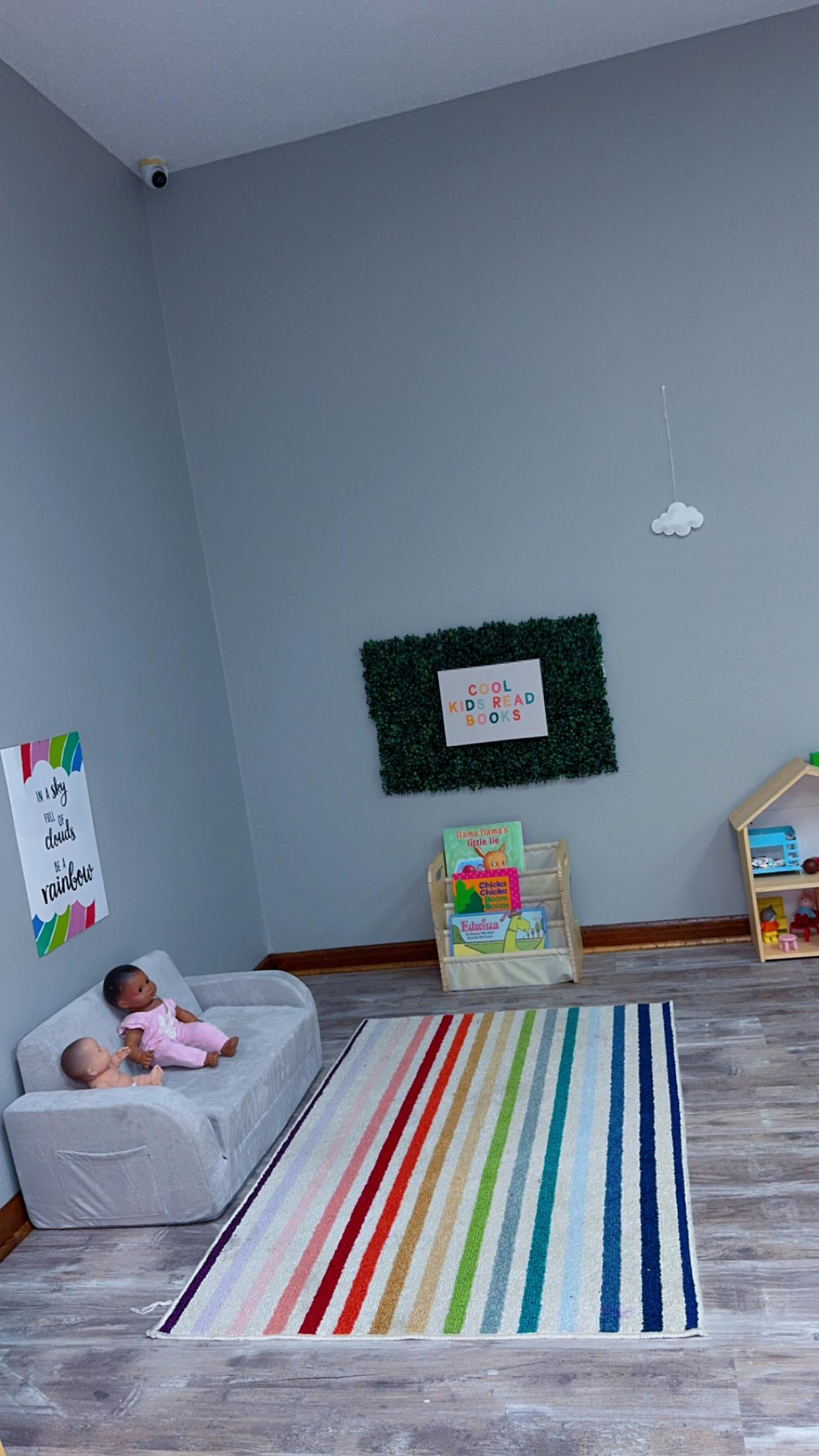 two dolls on a gray child-sized sofa with a striped rug on the floor