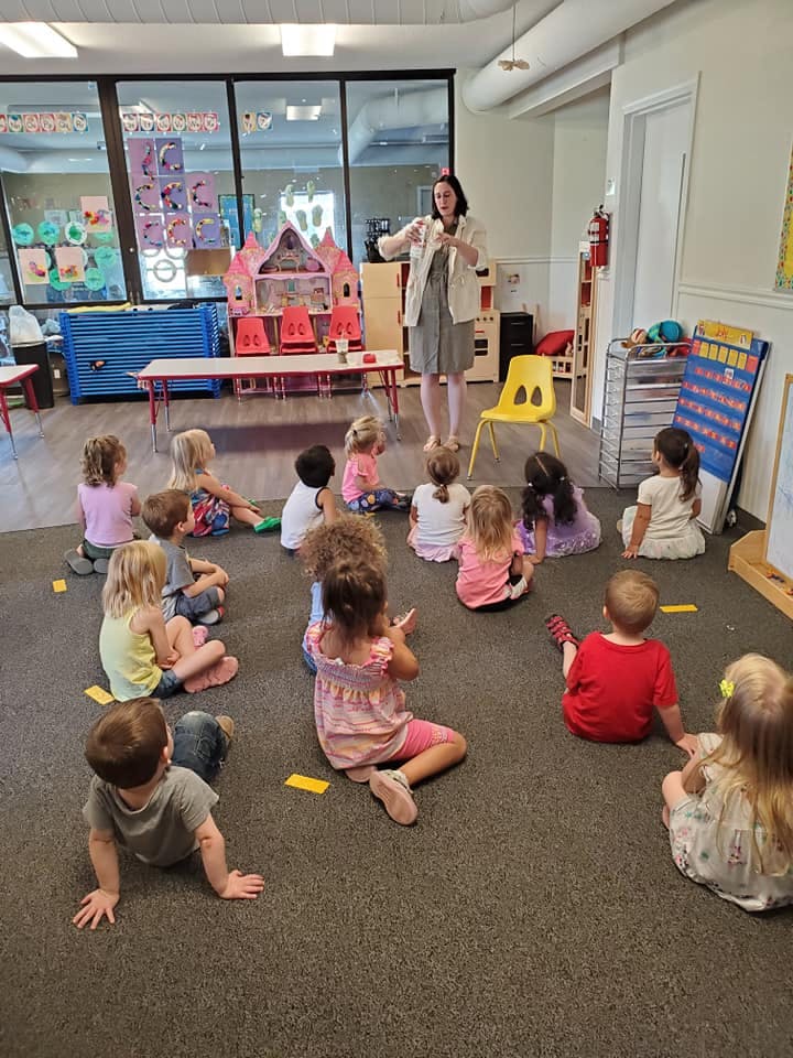 Adult person standing in front of children sitting on the floor in a classroom