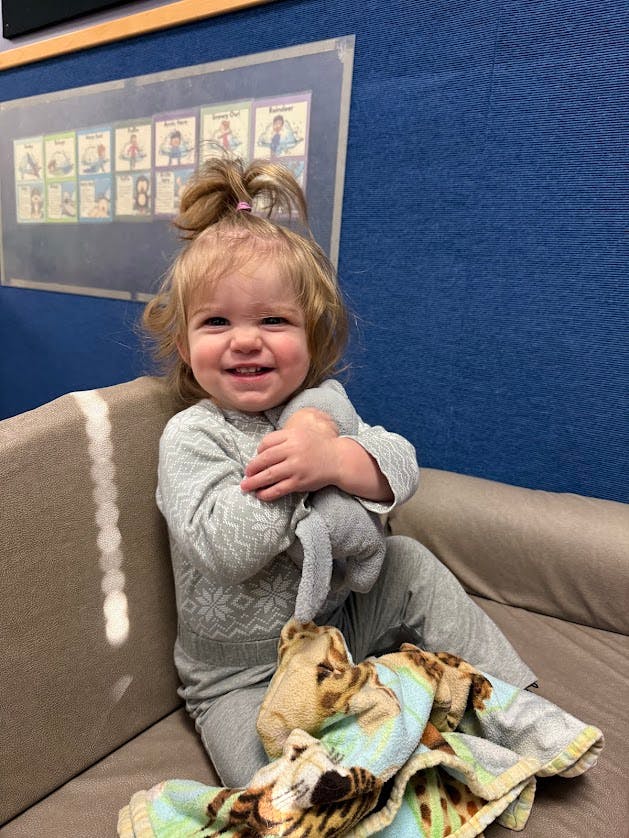 Smiling child with hair in a top bun holding a stuffed animal