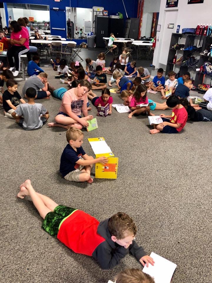 Many children sitting and lying on a carpeted floor reading books