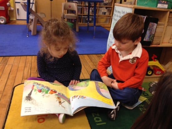 Two children sitting on a rug looking at an open book