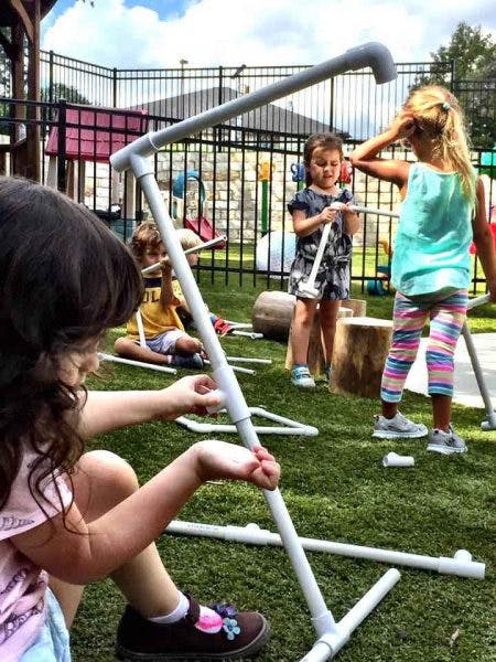 Children playing with PVC pipes on a grassy area
