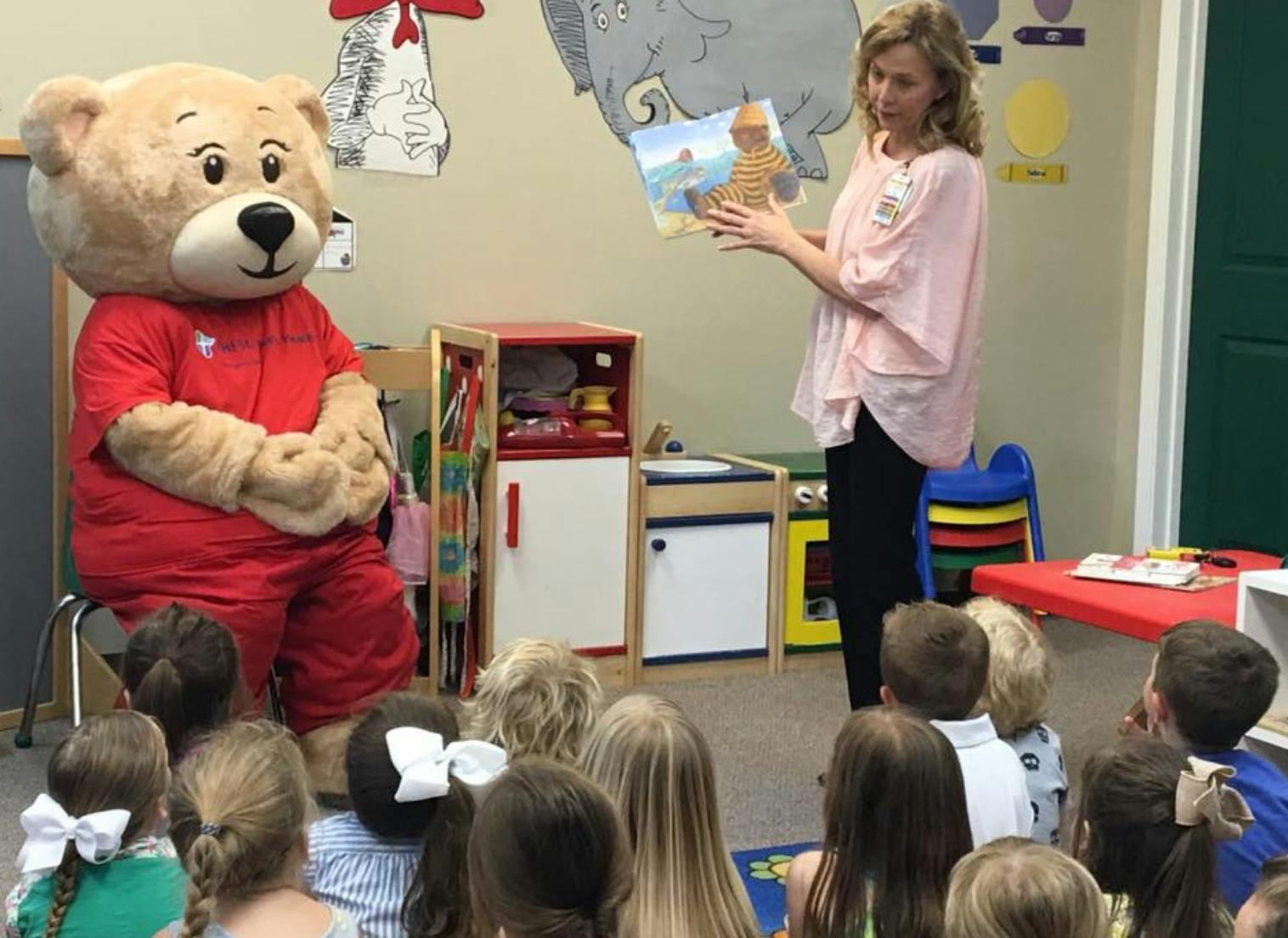 Person in bear costume and person reading to children