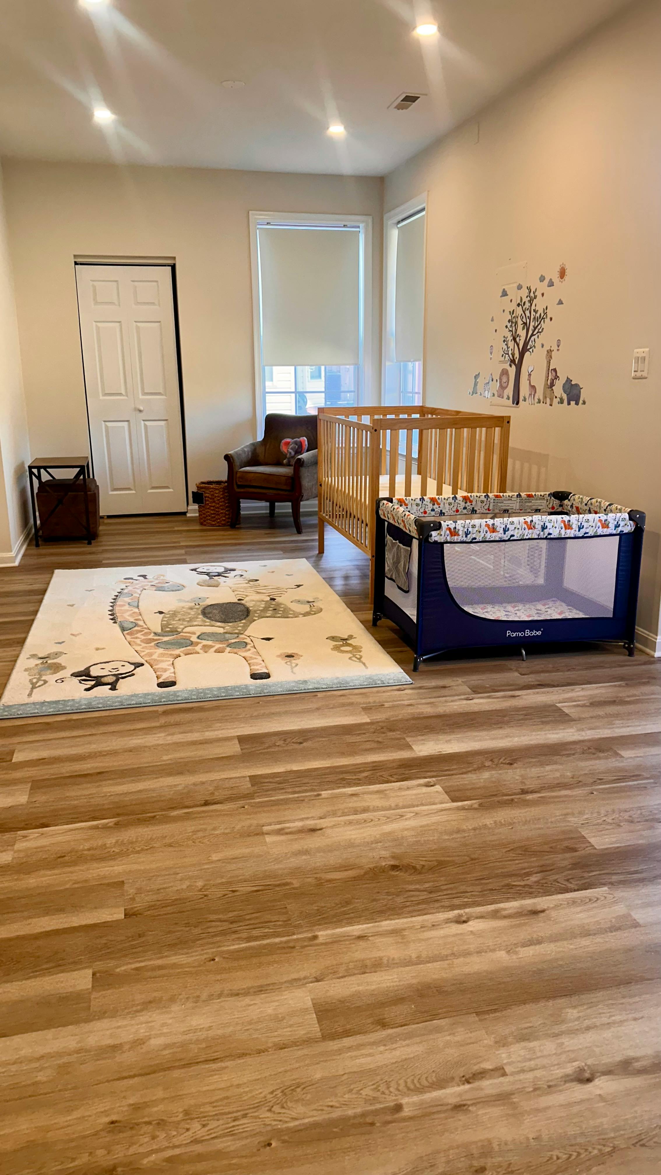 Nursery room with a wooden crib, a playpen, and a rug with animal designs