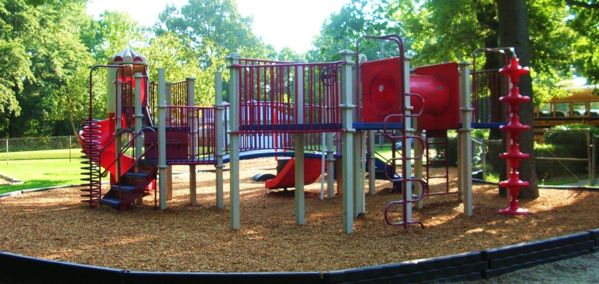 Playground with red slides and climbing structures on wood chips