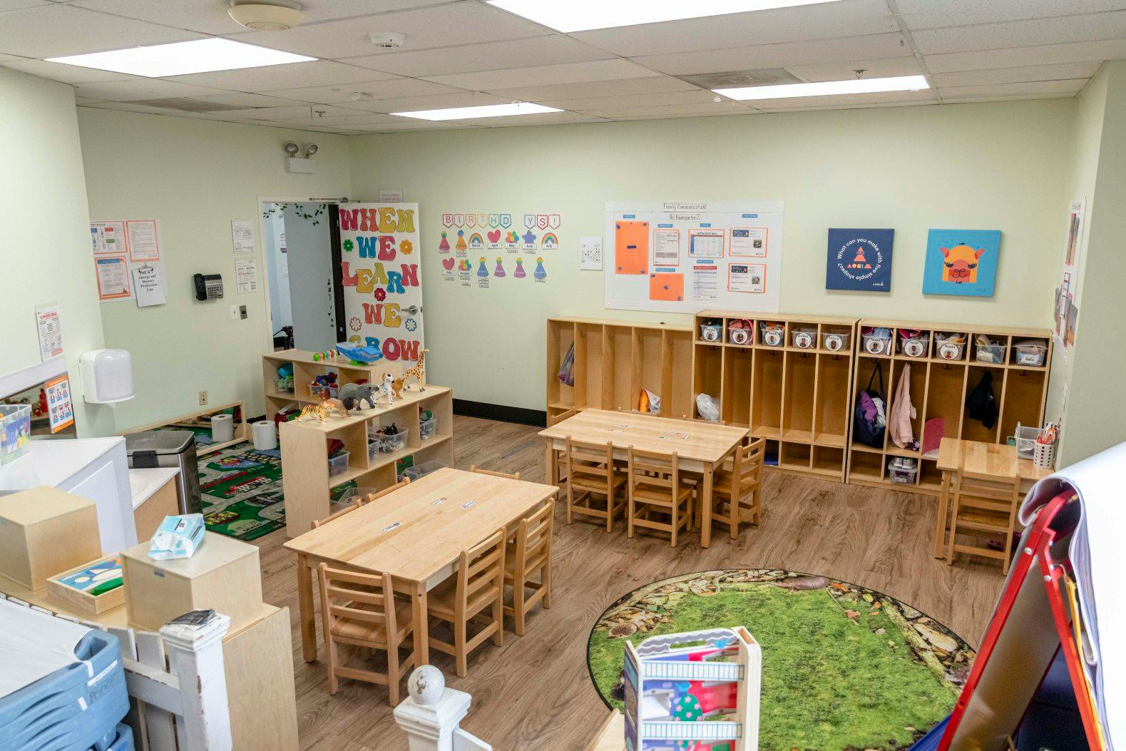 An empty classroom with small tables and chairs, shelves, and colorful wall decorations