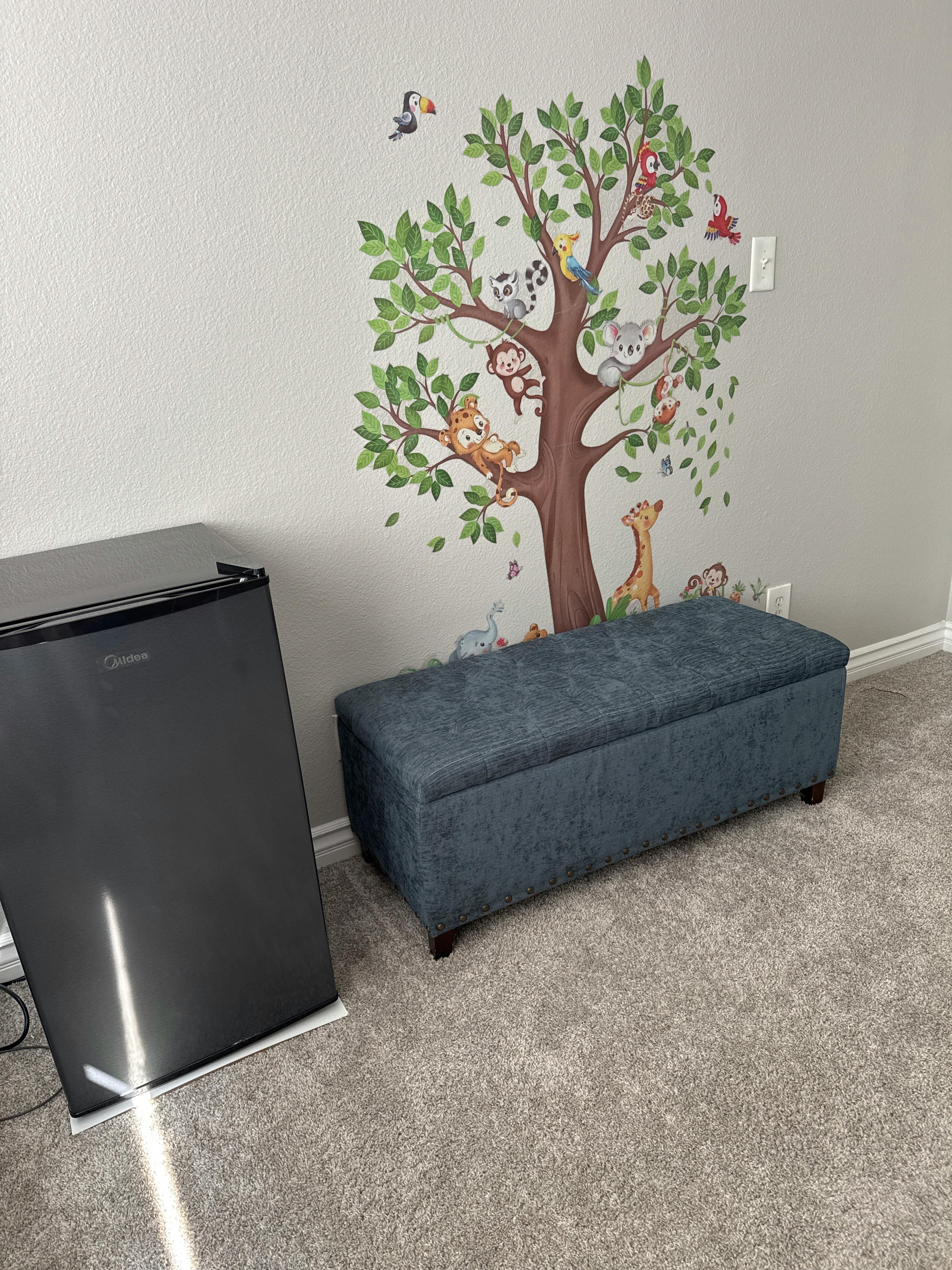 Animal tree wall decal next to a blue bench and mini refrigerator