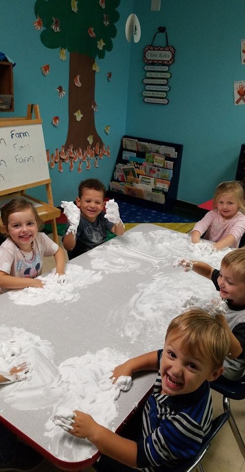 Children playing with shaving cream at a table in a classroom