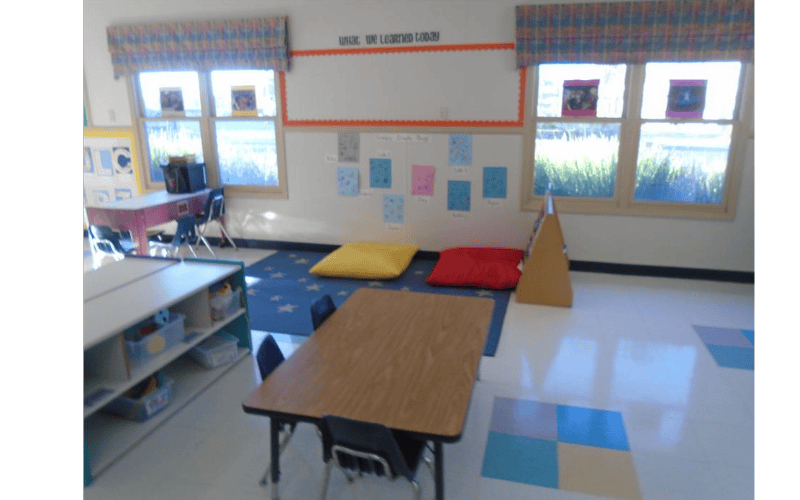 Classroom with tables, a rug with cushions, and windows
