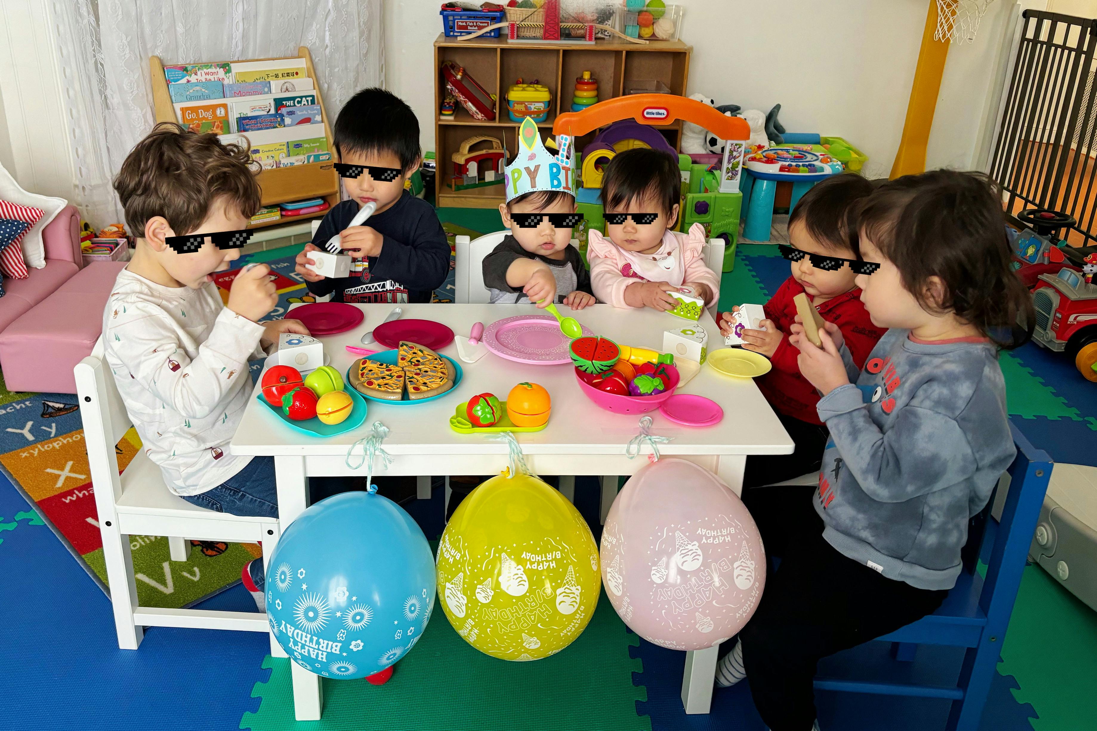 Children wearing sunglasses at a table with toy food and balloons