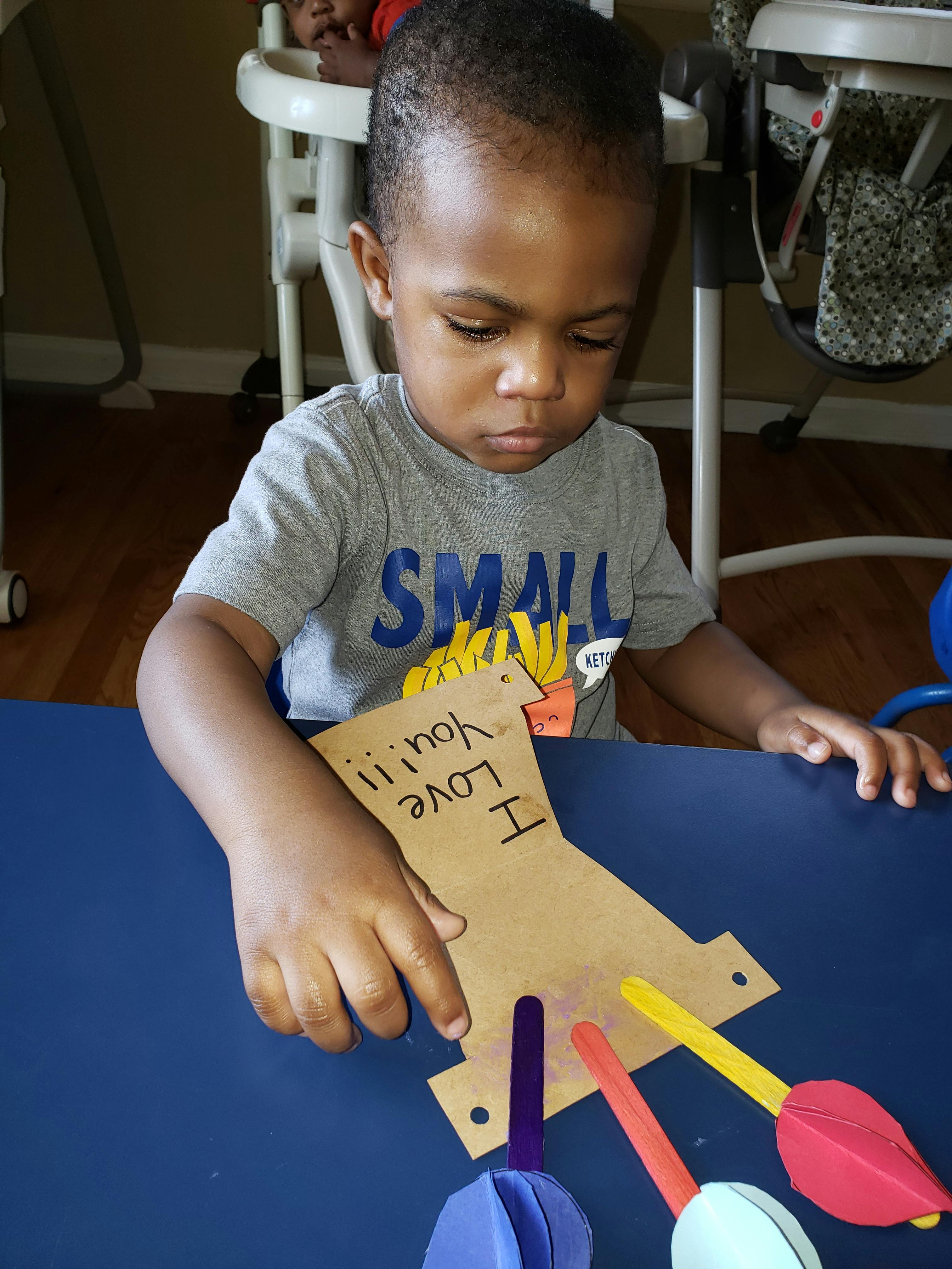 Child holding a paper craft with "I Love You" written on it