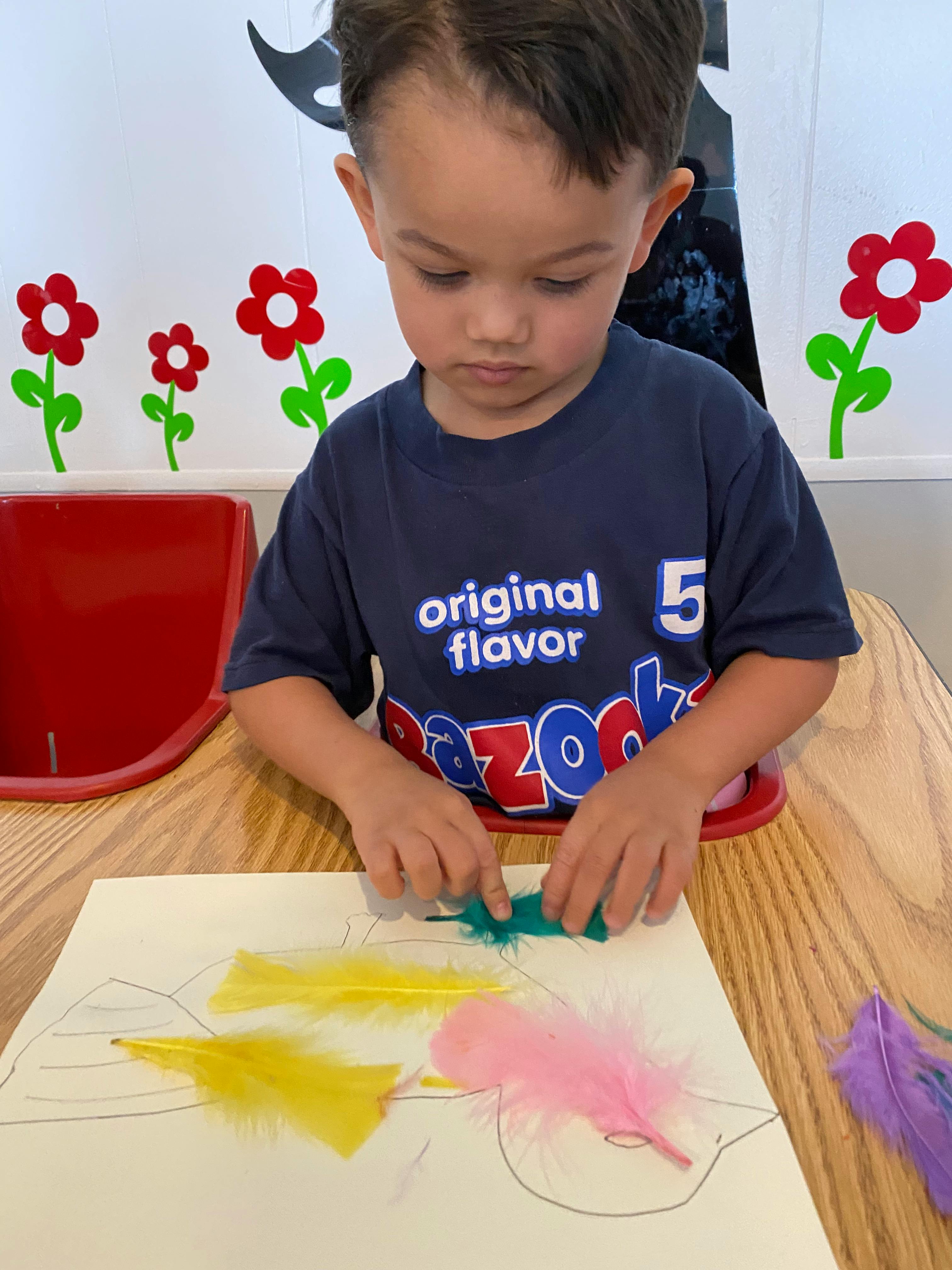 Child at a table working on a craft with feathers