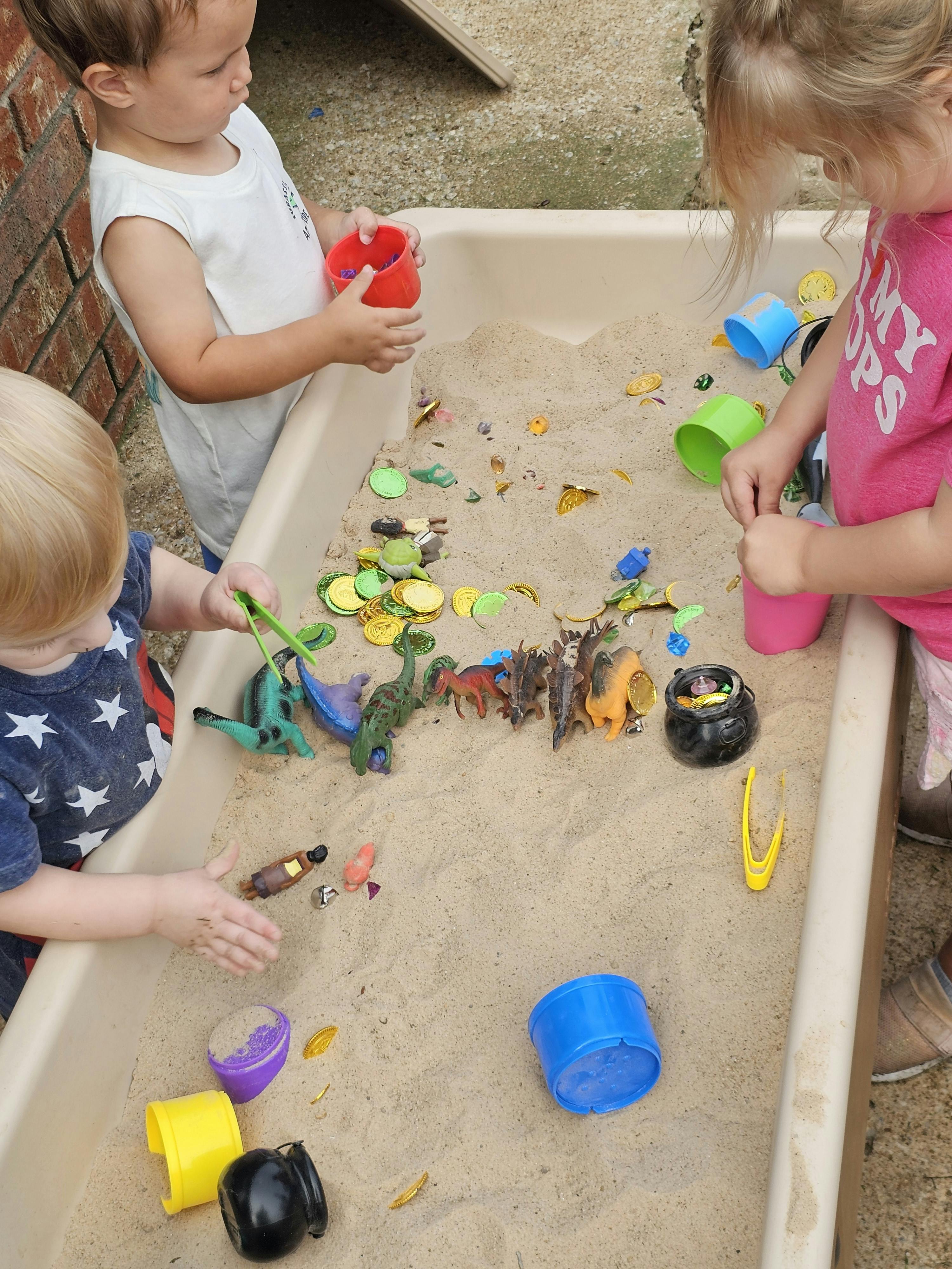 Three children playing in a sand table with toys