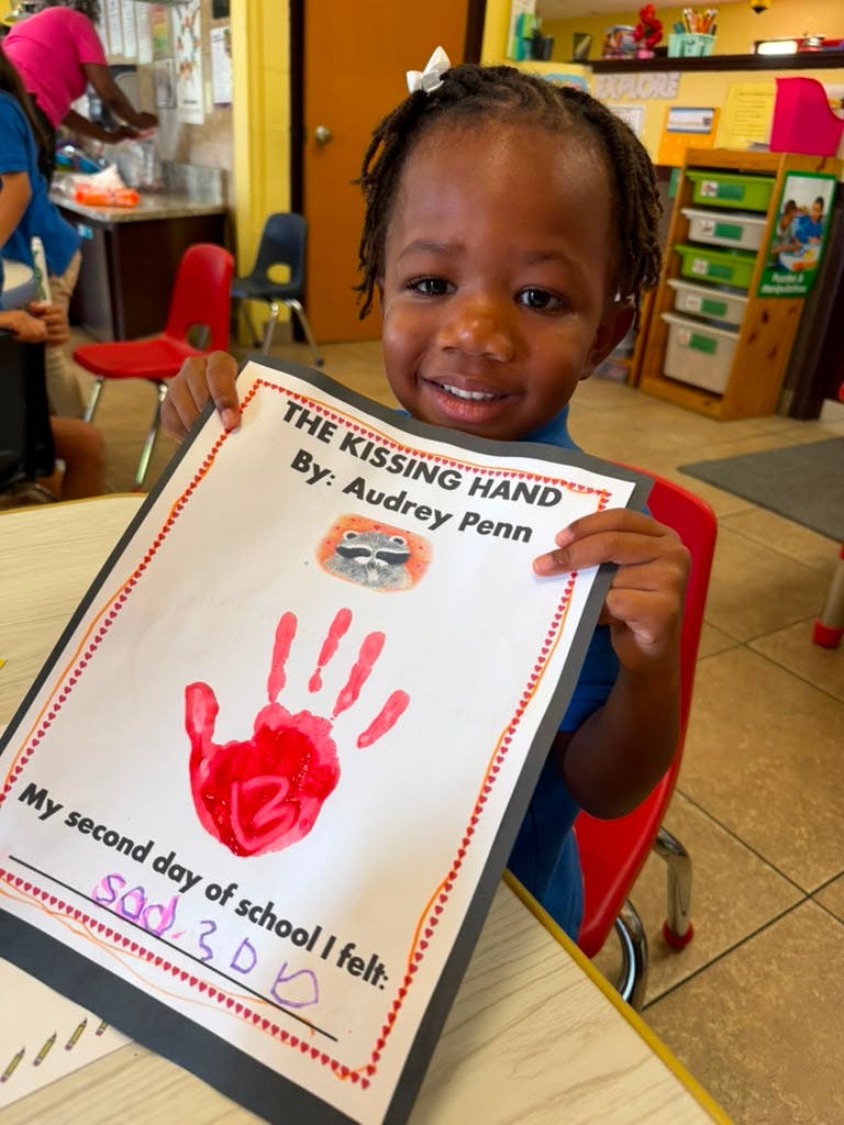Child holding a paper with a handprint and text about their second day of school