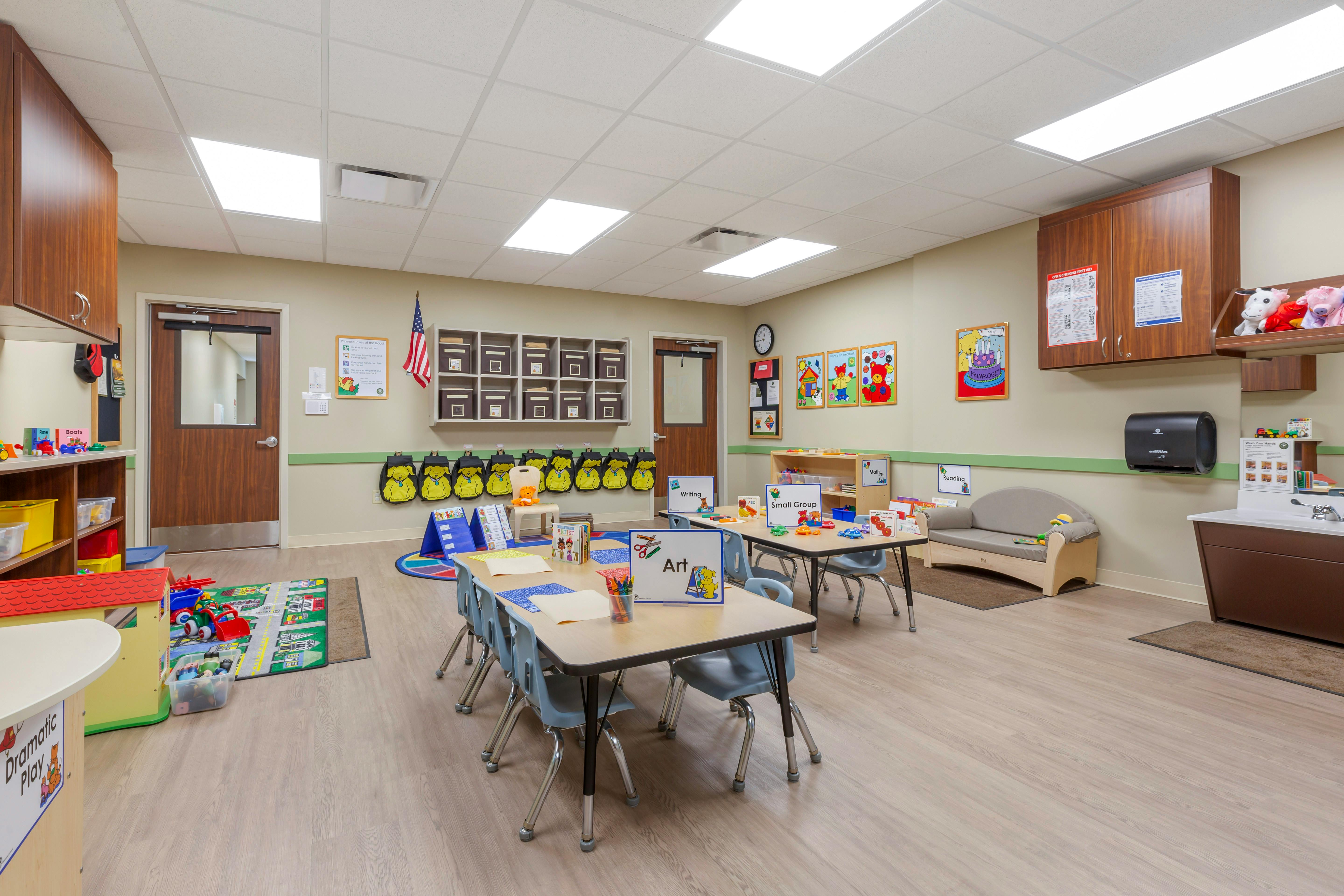 Empty classroom with tables, chairs, play areas, and educational posters on the walls