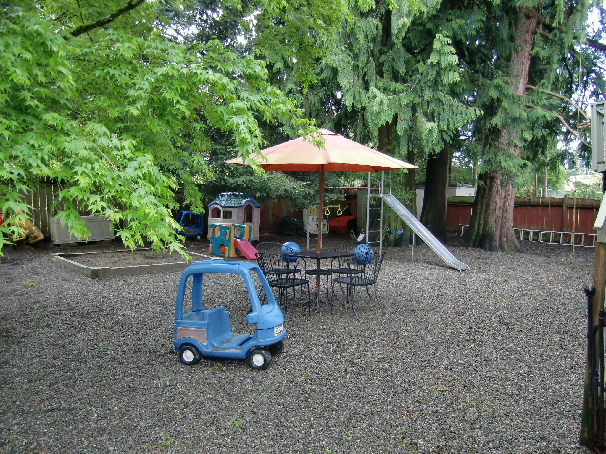 Playground with a blue toy car, umbrella, table, chairs, and slide