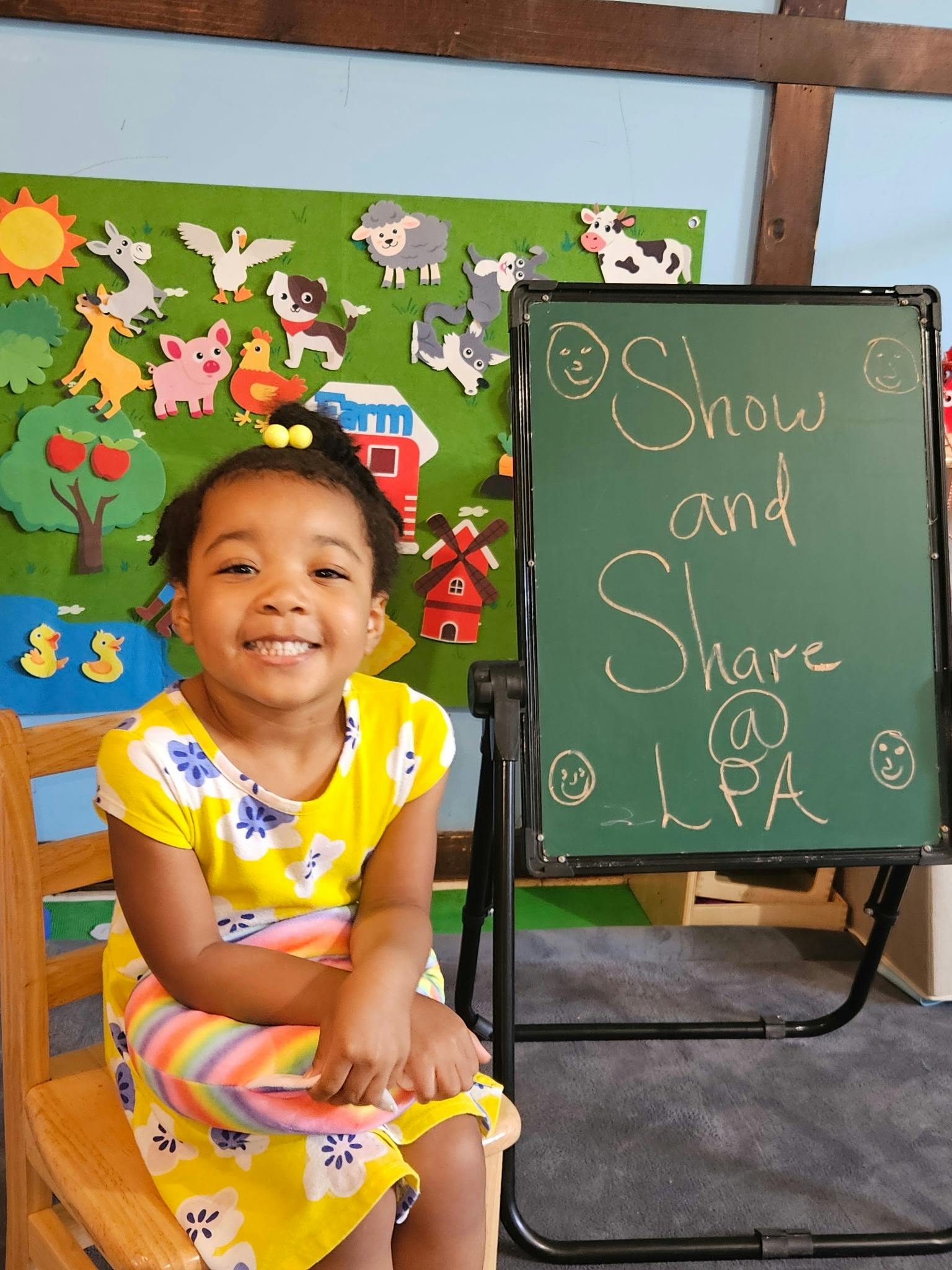 Child sitting next to a chalkboard reading Show and Share at LPA