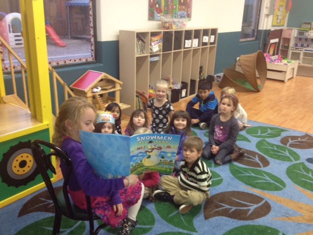 Child reading a book to a group of children in a classroom
