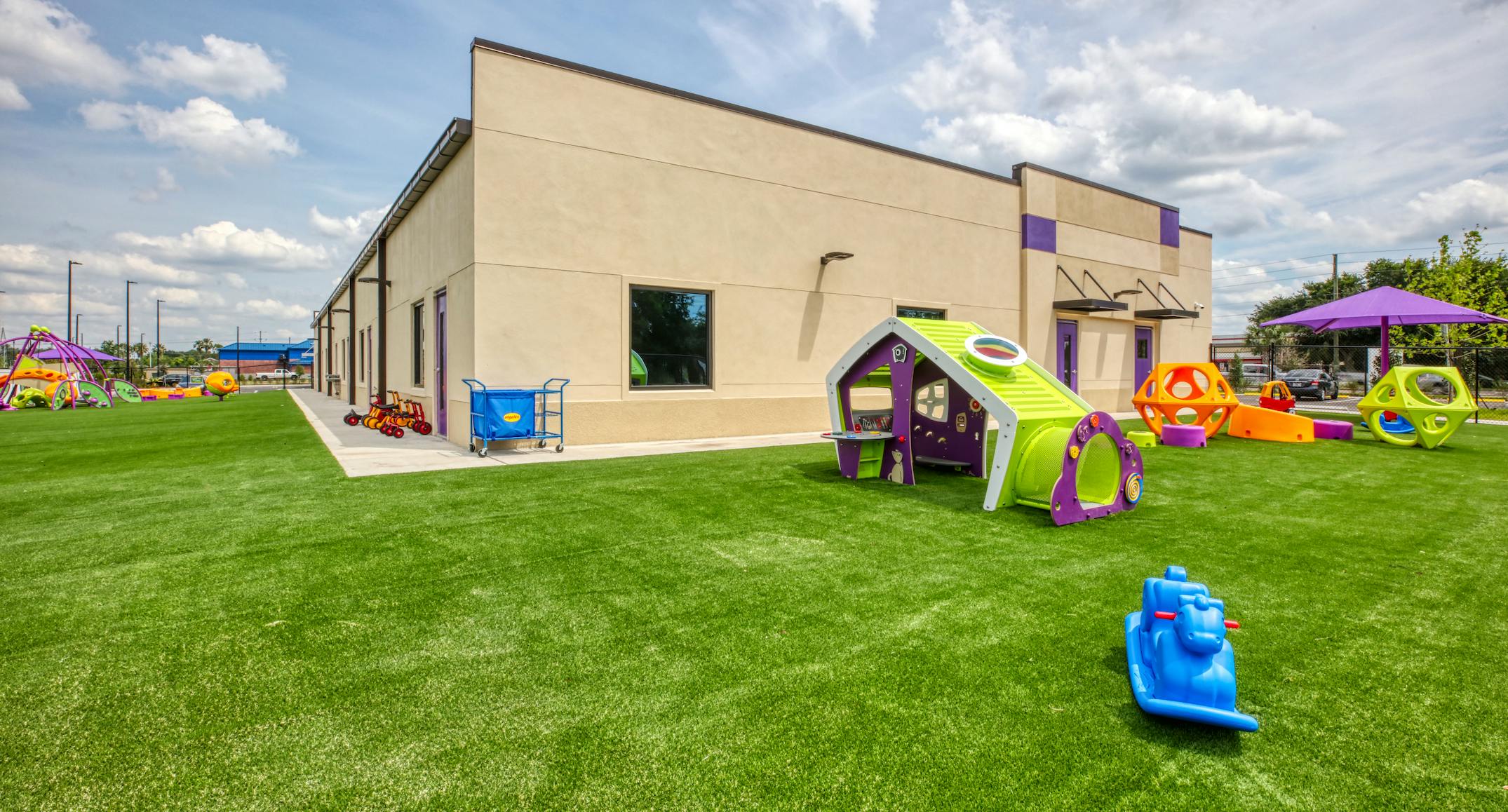 Playground with various play structures on artificial turf outside a building