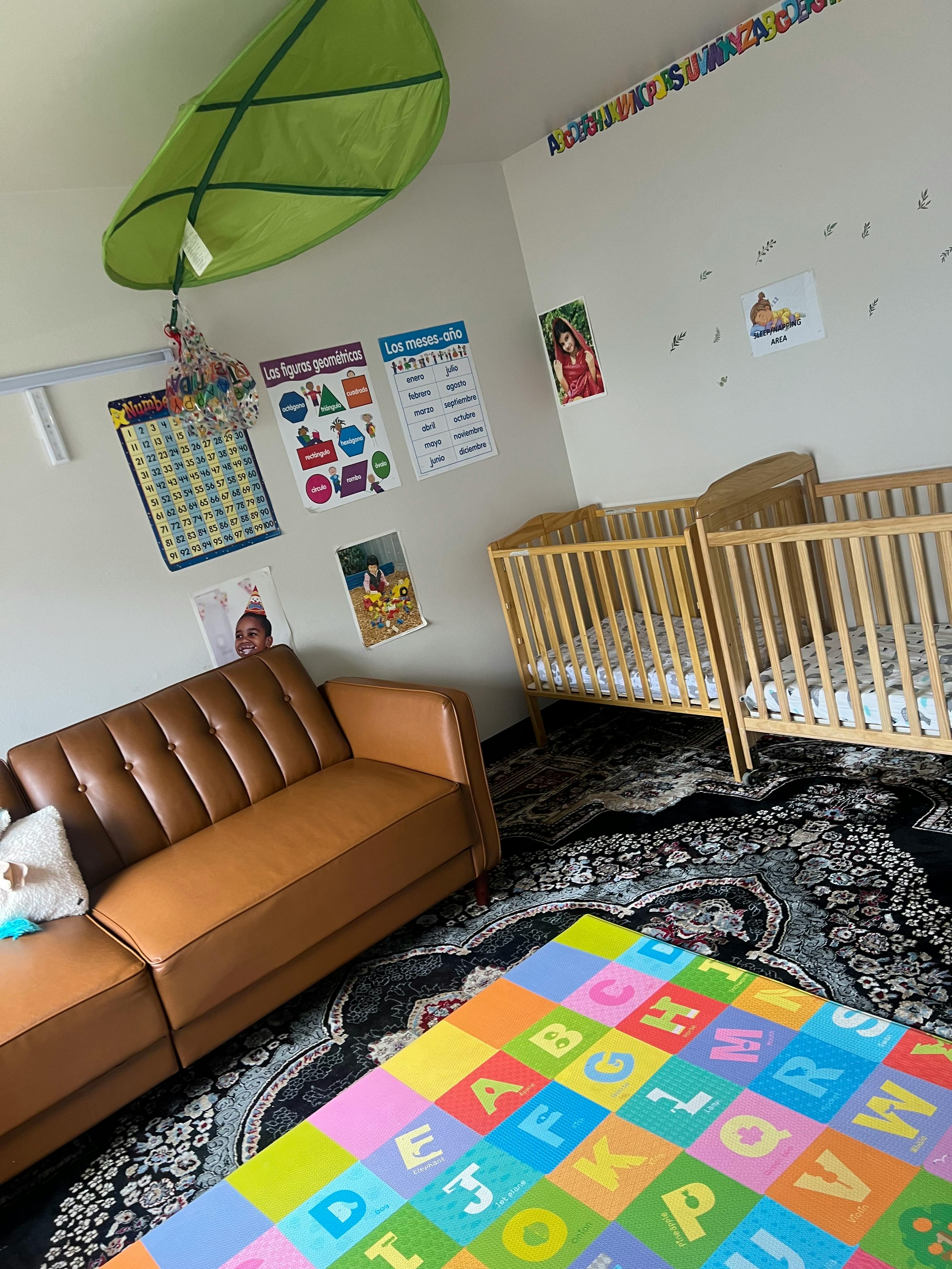 Two cribs and a brown sofa in a room with an alphabet playmat