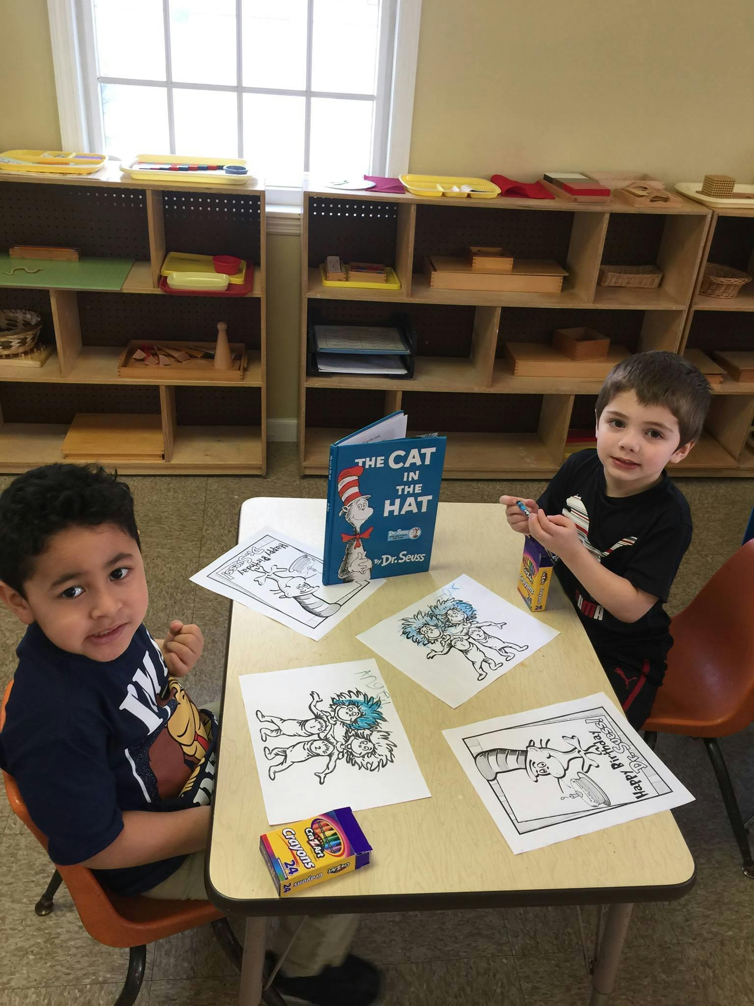 Two children at a table with coloring pages and "The Cat in the Hat" book