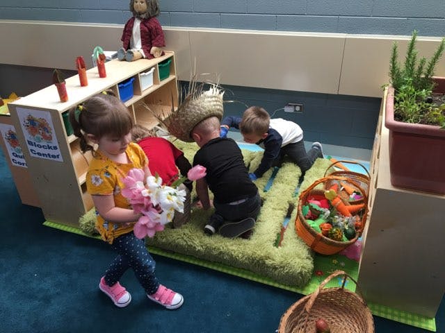 Child holding flowers while other children play on a mat